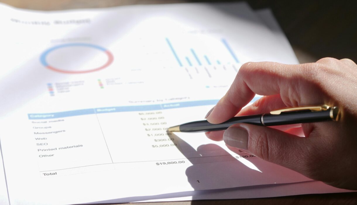 Hand holding pen, analyzing budget with charts and graph paper.